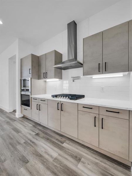 Kitchen with appliances with stainless steel finishes, wall chimney range hood, light wood-type flooring, and tasteful backsplash