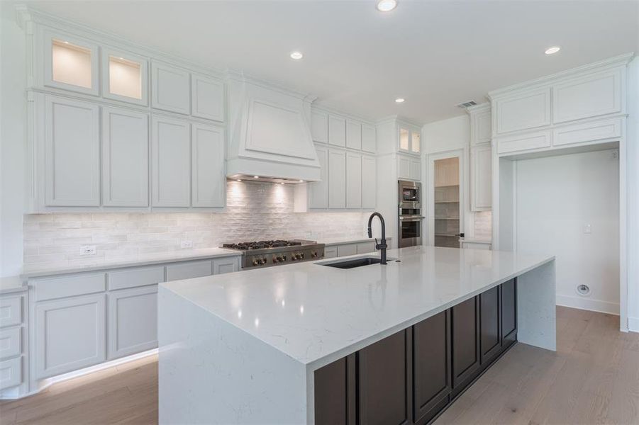 Kitchen with light hardwood / wood-style flooring, white cabinets, a kitchen island with sink, and sink