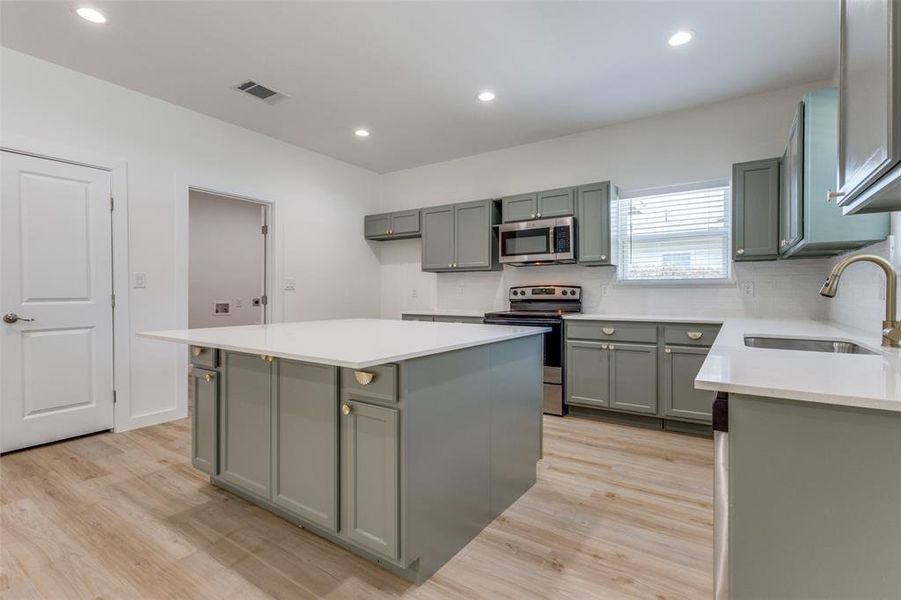 Kitchen featuring stainless steel appliances, sink, backsplash, light hardwood / wood-style floors, and a center island