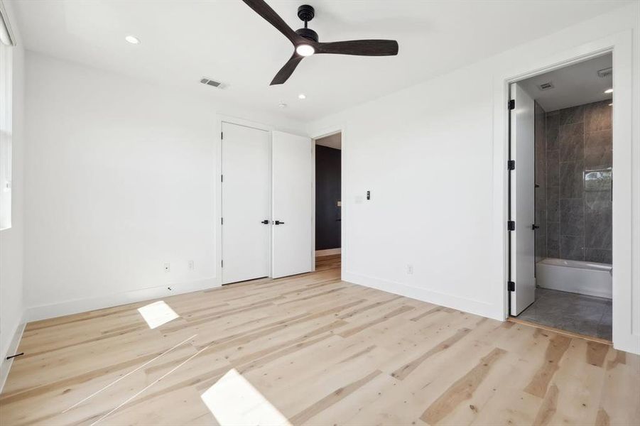 Unfurnished bedroom featuring a closet, ensuite bath, ceiling fan, and light wood-type flooring