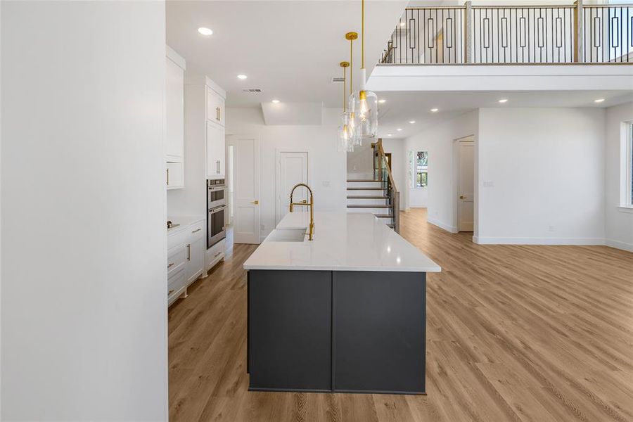 Kitchen with white cabinetry, a large island with sink, light hardwood / wood-style flooring, and hanging light fixtures