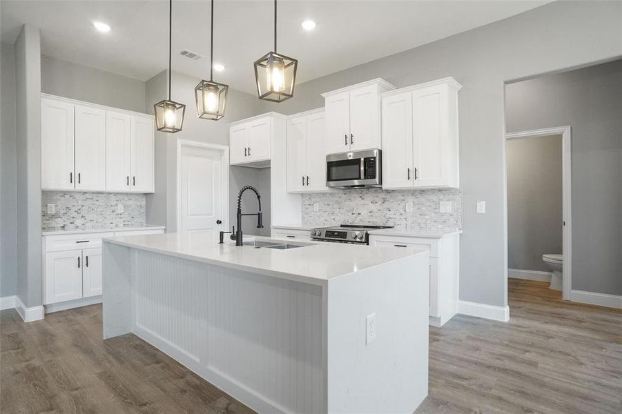 Kitchen featuring backsplash, stainless steel appliances, light hardwood / wood-style floors, and an island with sink