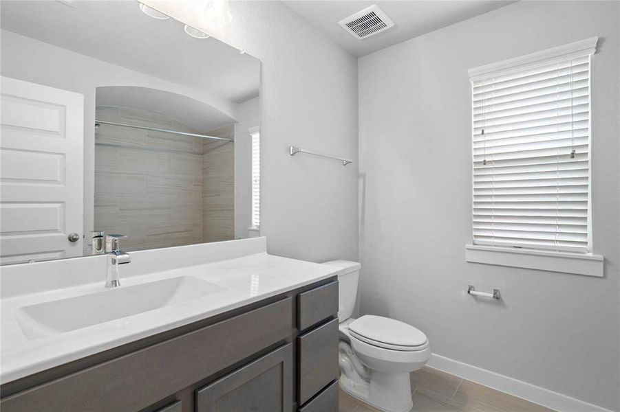 Secondary bathroom features light countertops and stained cabinets, neutral paint, shower/tub combo with tile surround, large mirror, tile floors, sleek fixtures and modern finishes.