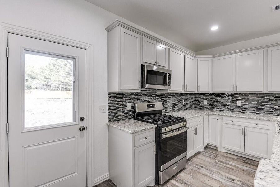 Kitchen featuring backsplash, white cabinetry, appliances with stainless steel finishes, light stone counters, and light hardwood / wood-style floors