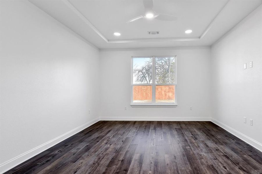 Empty room with dark wood-type flooring, a tray ceiling, and ceiling fan