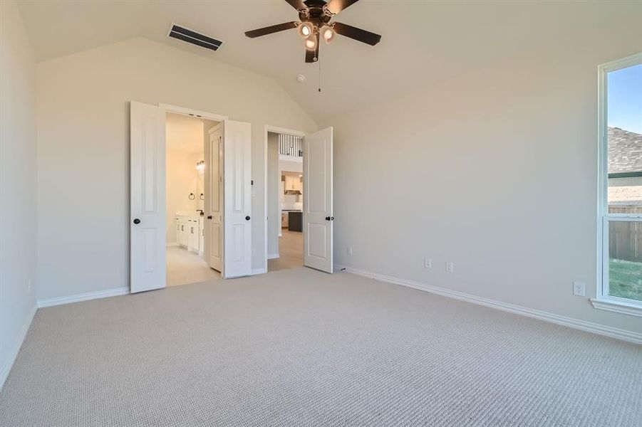 Unfurnished bedroom with connected bathroom, ceiling fan, lofted ceiling, and light colored carpet