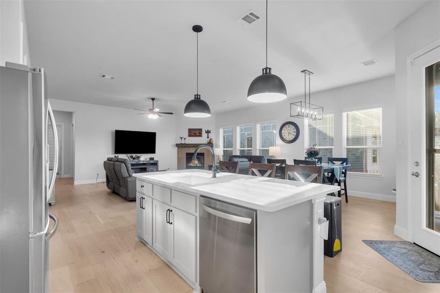 Kitchen featuring stainless steel appliances, decorative light fixtures, an island with sink, and light wood-style floors