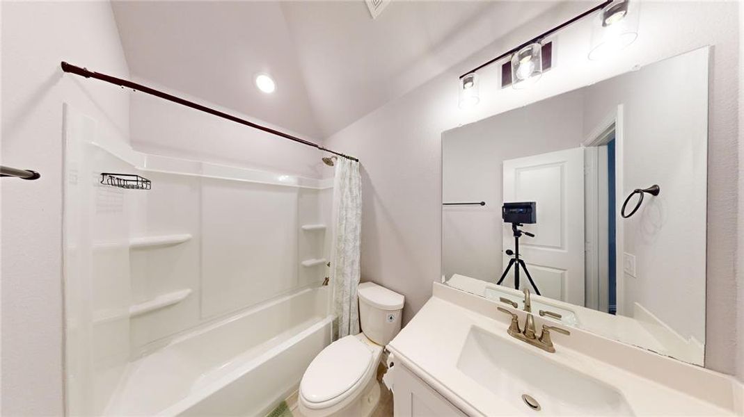 Full bathroom with shower / tub combo, lofted ceiling, vanity, and toilet