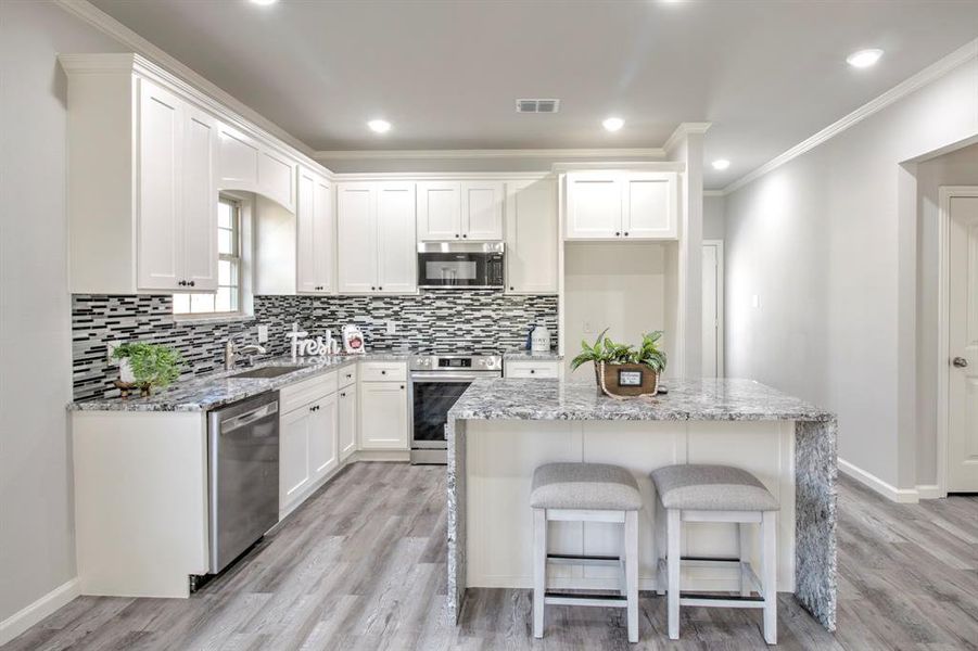 Kitchen featuring white cabinetry, appliances with stainless steel finishes, light stone countertops, and a center island