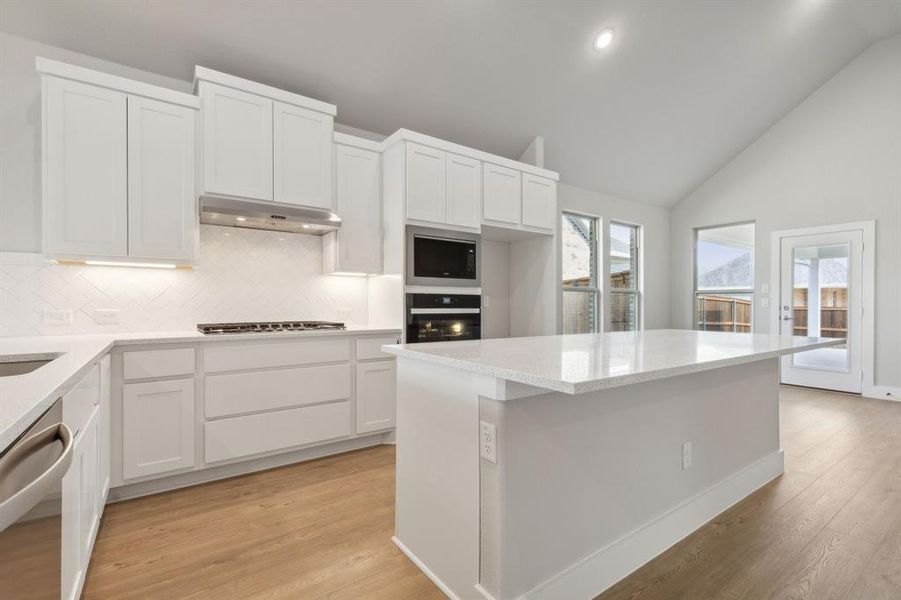 Kitchen with stainless steel appliances, white cabinets, decorative backsplash, a kitchen island, and light hardwood / wood-style flooring