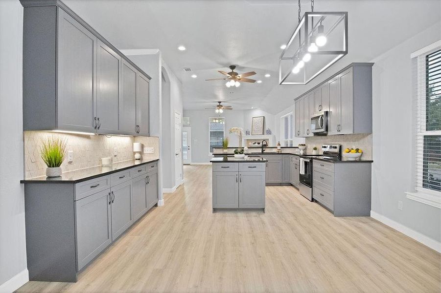 Kitchen with gray cabinets, black granite countertops, stainless steel appliances, tasteful backsplash, and light laminate wood-type flooring throughout.