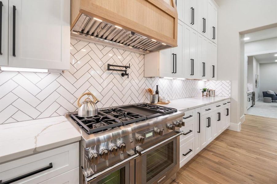 Kitchen with white cabinetry, double oven range, custom exhaust hood, and light hardwood / wood-style floors