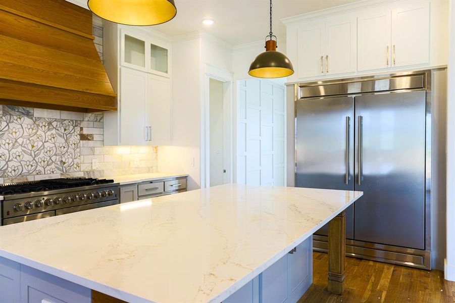 Kitchen with premium appliances, tasteful backsplash, white cabinets, dark wood-type flooring, and decorative light fixtures