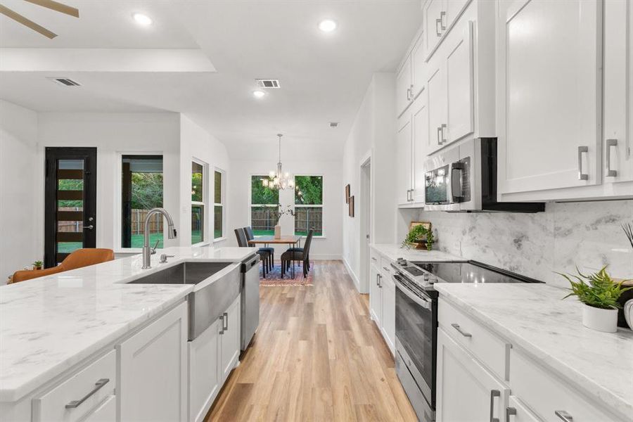 Kitchen featuring decorative backsplash, stainless steel appliances, sink, white cabinetry, and light hardwood / wood-style flooring