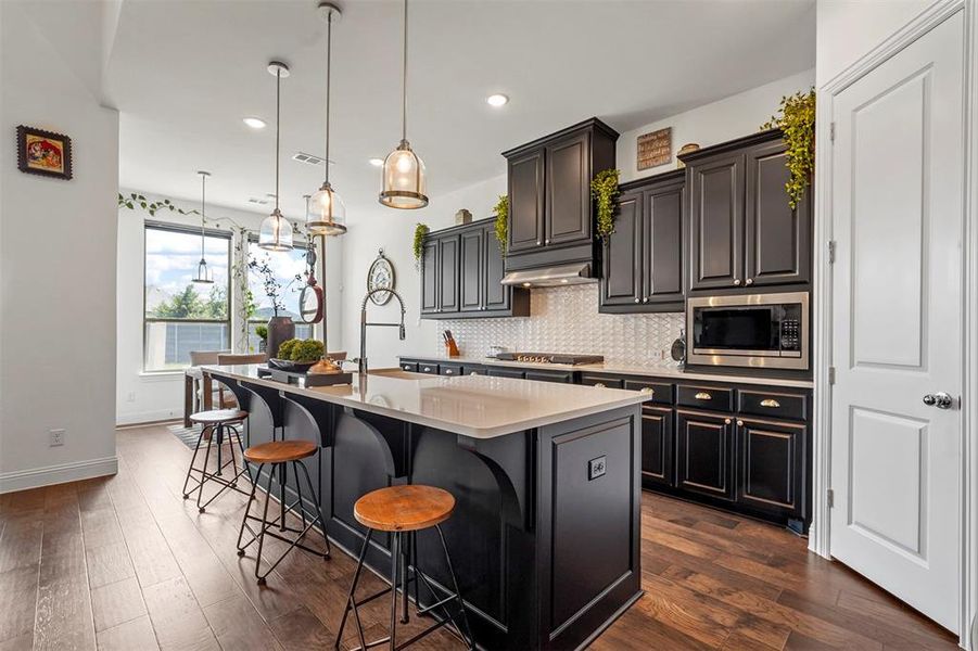Kitchen featuring stainless steel appliances, a kitchen bar, dark hardwood / wood-style floors, a center island with sink, and backsplash