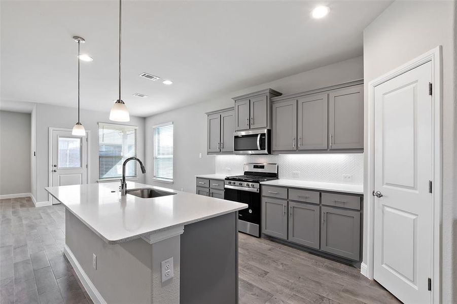 Kitchen featuring light hardwood / wood-style floors, decorative light fixtures, stainless steel appliances, and sink