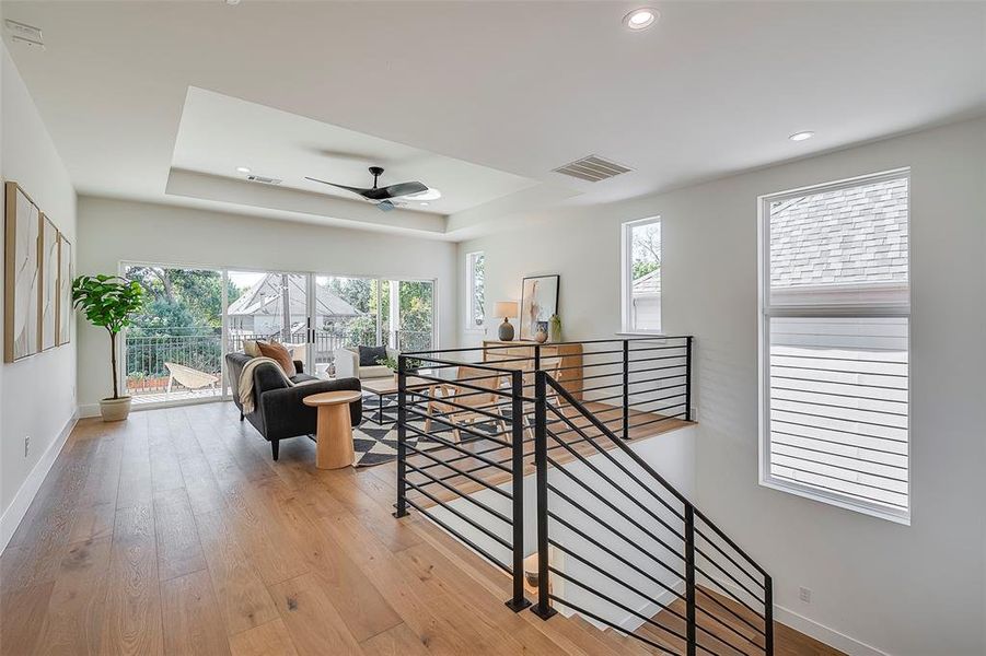 Corridor featuring a tray ceiling, a healthy amount of sunlight, and light wood-type flooring