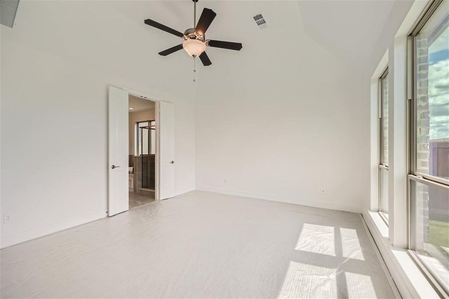 Spare room with a healthy amount of sunlight, light carpet, high vaulted ceiling, and ceiling fan