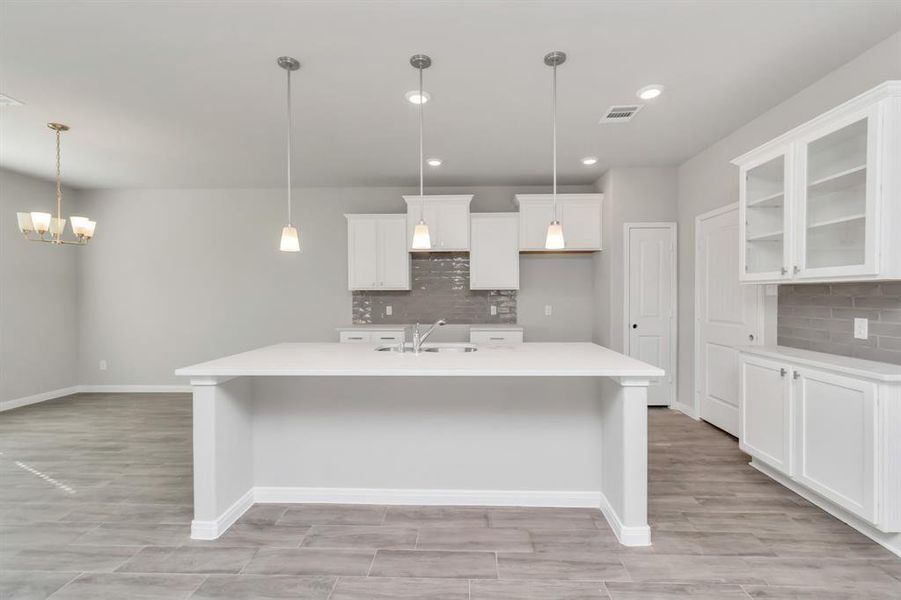 The open-concept kitchen seamlessly connects with the dining area, offering a perfect setup for hosting family and friends. The spacious island provides additional seating and workspace, while the modern lighting fixtures create a warm, inviting atmosphere. This well-designed space combines form and function, making it the heart of the home. **This image is from another Saratoga Home with similar floor plan and finishes, not the June floorplan.**