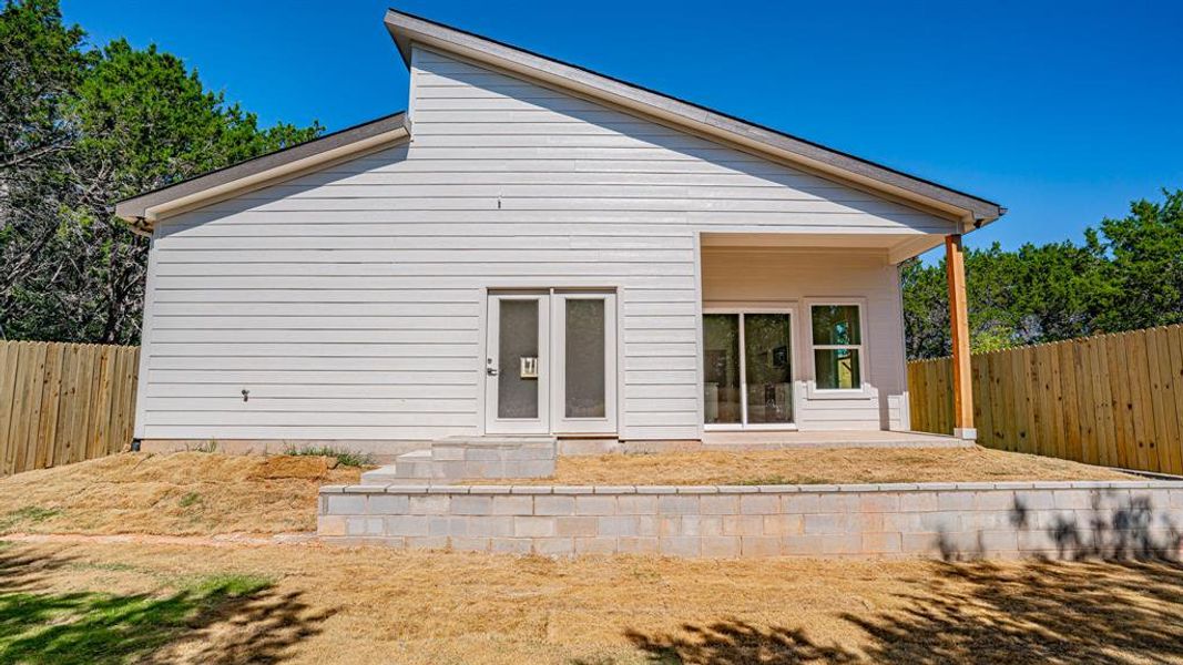 Rear view of home with double doors from the dining room and primary bedroom. Retaing wall, sodded yard and privacy fence