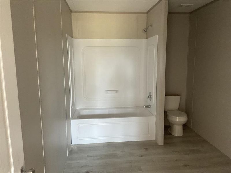 Bathroom with shower / bath combination, hardwood / wood-style floors, and toilet