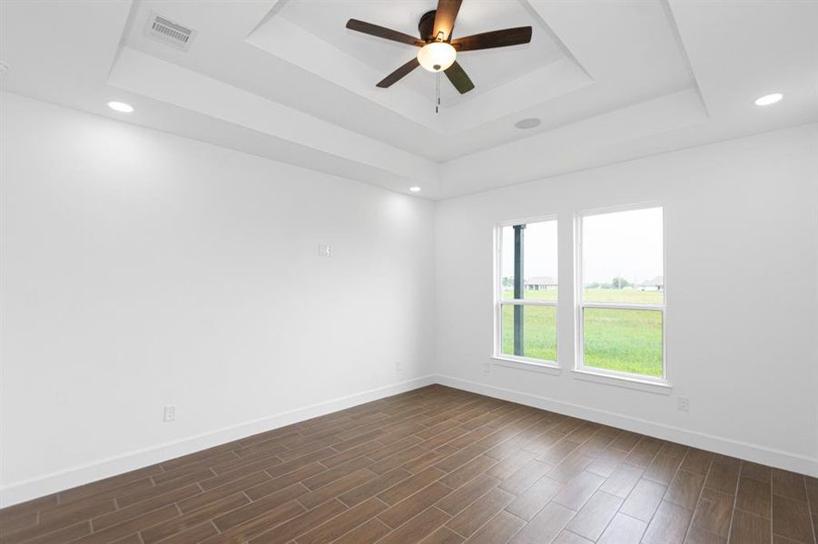 Primary bedroom with a view to the backyard through the oversized windows that allow natural lighting.  This beautiful bedroom has tiered ceilings, recessed lighting, ceiling fan, and a BLUETOOTH AUDIO SPEAKER SYSTEM for the music enthusiast.