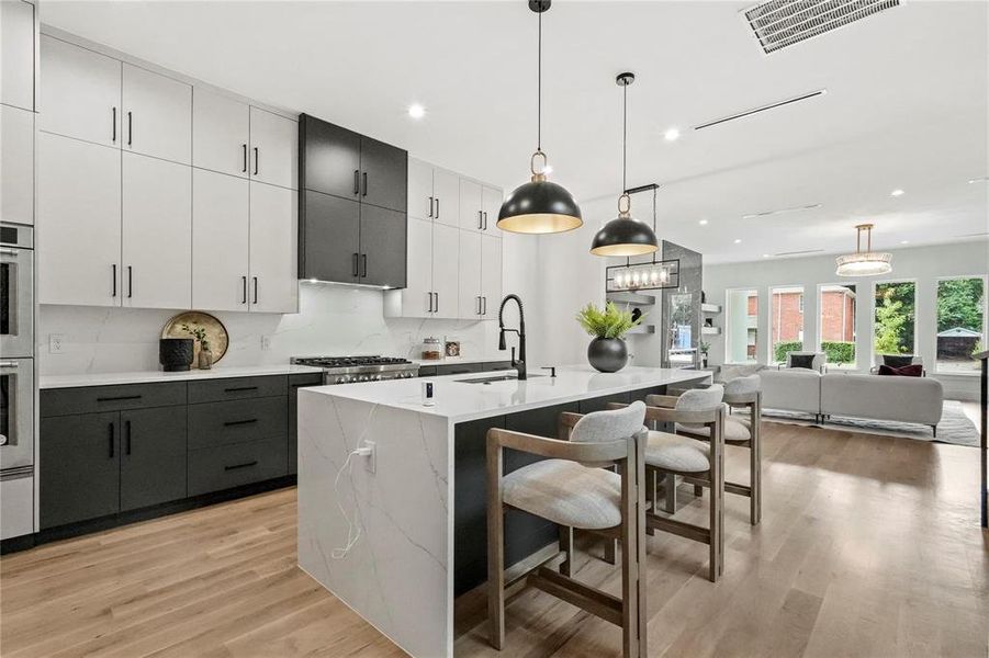 Kitchen with decorative backsplash, an island with sink, light hardwood / wood-style flooring, sink, and pendant lighting