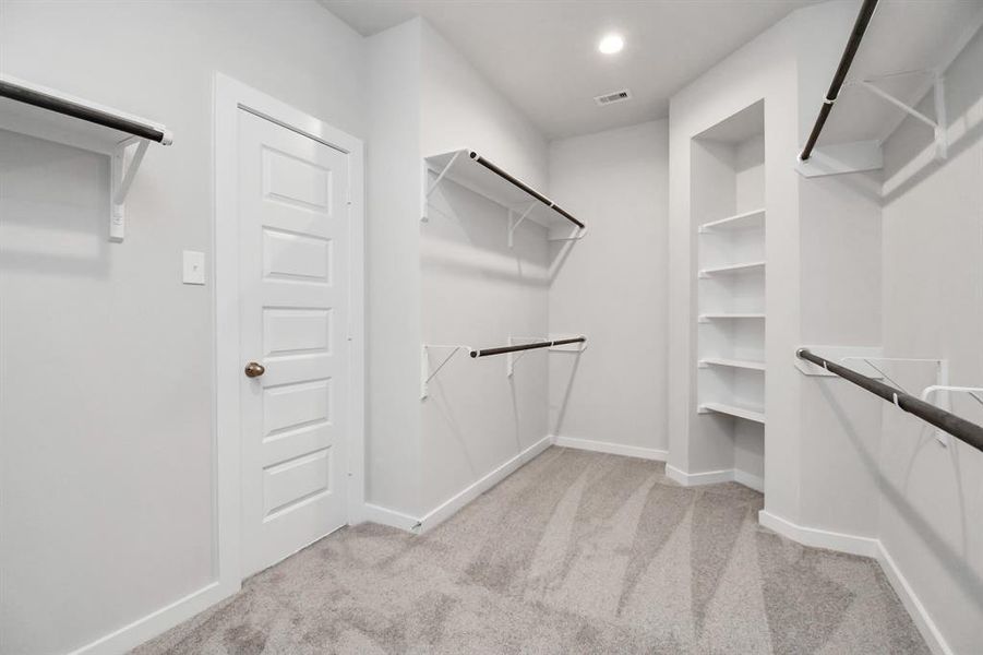 This generously sized closet boasts built-in shelving, providing ample room for organization. With high ceilings and recessed lighting, the ambiance is both bright and welcoming. Plush carpeting underfoot enhances the comfort, while warm paint tones add a touch of coziness.