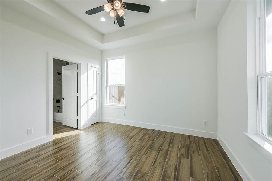 This is a bright, modern room featuring high ceilings with a ceiling fan, large windows for natural light, and stylish wood flooring. There's also a view into another room or closet with a unique door design.