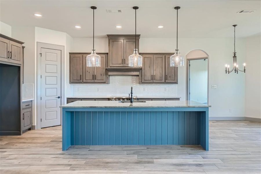 Kitchen featuring sink, light hardwood / wood-style flooring, hanging light fixtures, and a center island with sink