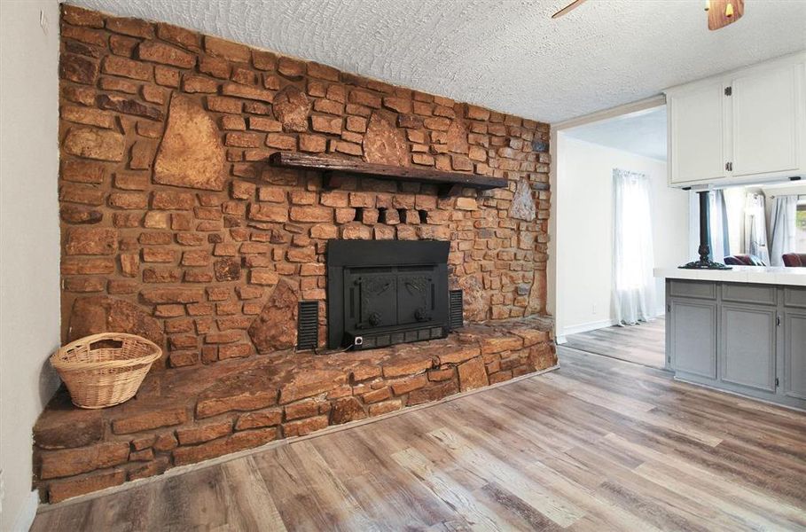 Unfurnished living room with light hardwood / wood-style floors, a textured ceiling, and a stone fireplace