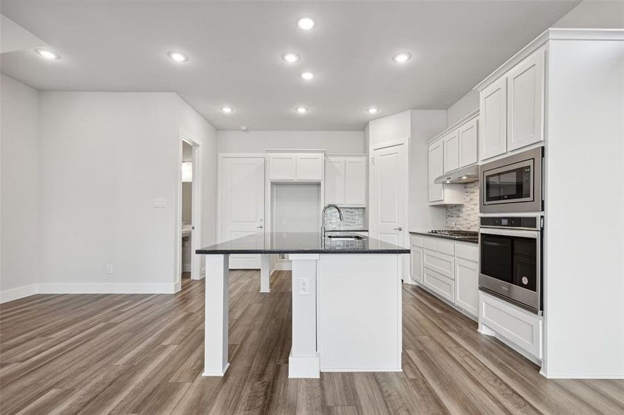 Kitchen featuring stainless steel appliances, a center island with sink, hardwood / wood-style floors, and backsplash