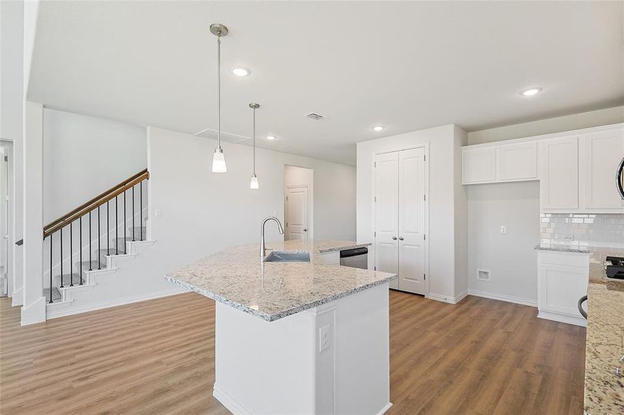 Kitchen featuring white cabinets, an island with sink, decorative light fixtures, and light hardwood / wood-style flooring