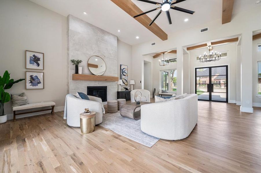 Living room with light hardwood / wood-style flooring, a large fireplace, ceiling fan with notable chandelier, beam ceiling, and a towering ceiling