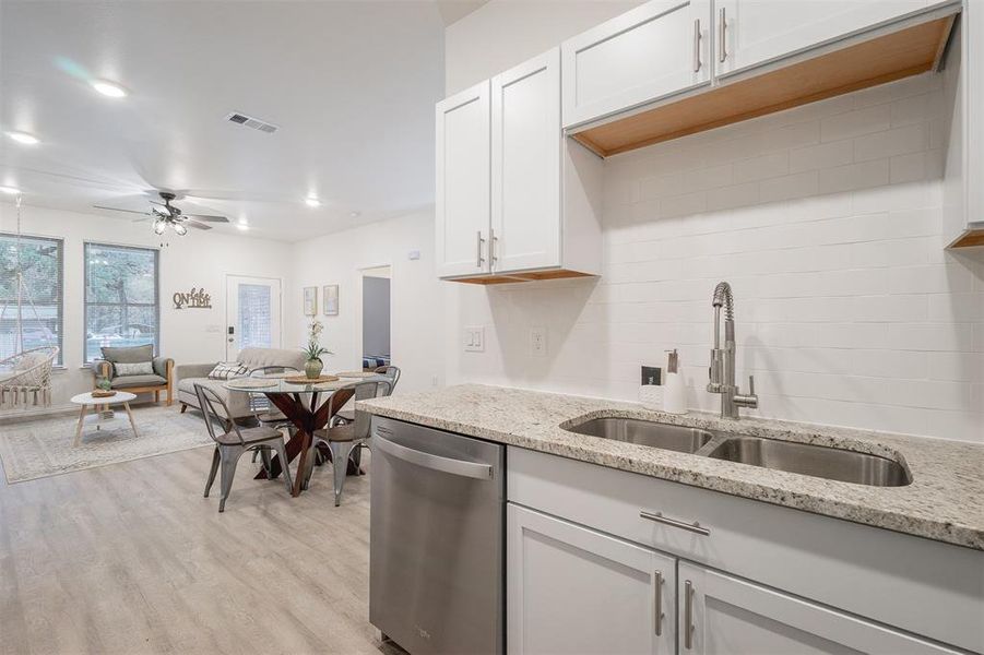 Kitchen featuring sink, light hardwood / wood-style flooring, white cabinetry, dishwasher, and light stone countertops