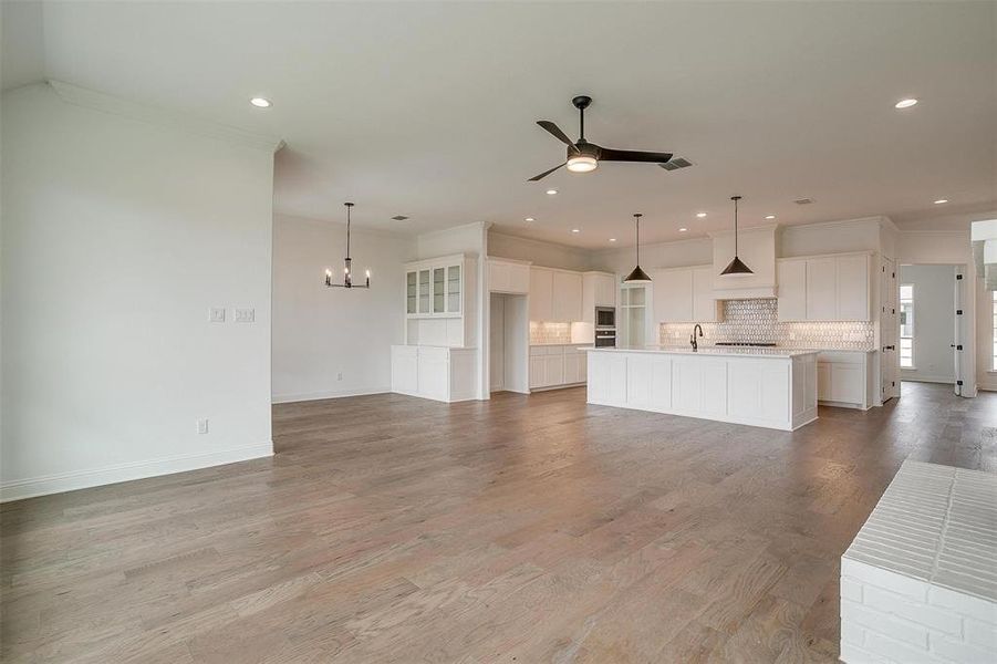 Unfurnished living room featuring ceiling fan with notable chandelier, ornamental molding, sink, and light wood-type flooring