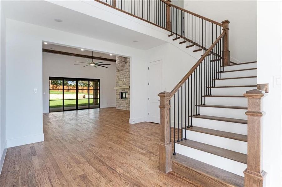 Stairway featuring brick wall, ceiling fan, hardwood / wood-style flooring, and a fireplace