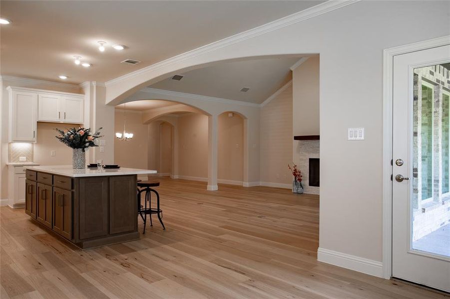 Kitchen featuring a center island with sink, backsplash, white cabinetry, light wood-type flooring, and crown molding