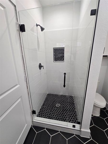 Bathroom featuring tile patterned flooring, walk in shower, and toilet