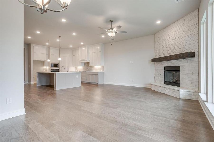 Unfurnished living room with ceiling fan with notable chandelier, sink, light hardwood / wood-style flooring, and a stone fireplace