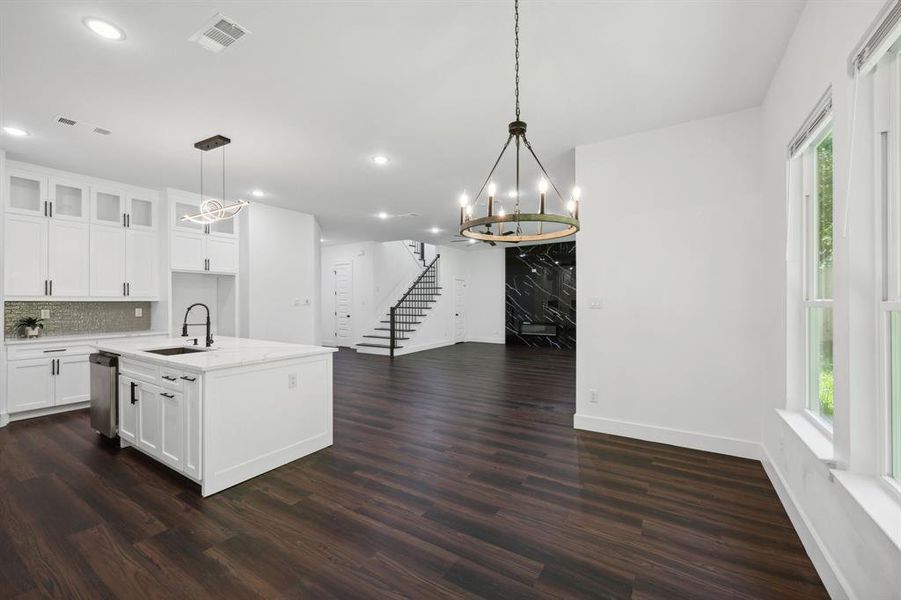 Kitchen featuring dark wood-type flooring, white cabinets, a kitchen island with sink, decorative light fixtures, and sink