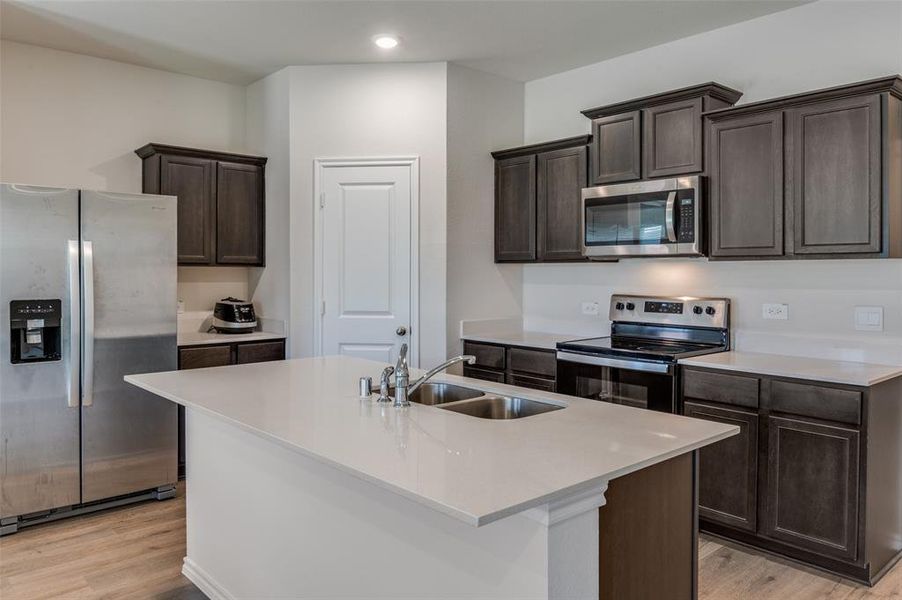 Kitchen with sink, appliances with stainless steel finishes, light hardwood / wood-style floors, and an island with sink