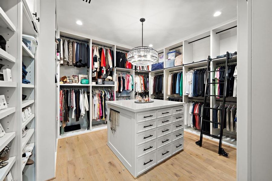 Indulge in this Elegant and Functional Primary Closet -features custom built-ins, island drawers with quartz countertops, a ladder for easy access to high storage, Pant wracks ,House of Savoy Crystal Chandelier and the continung of the European Style White Oak Floors.