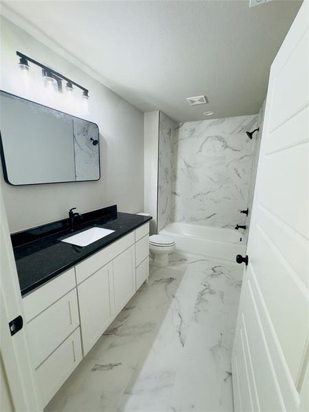 Full bathroom featuring vanity, tiled shower / bath combo, and toilet