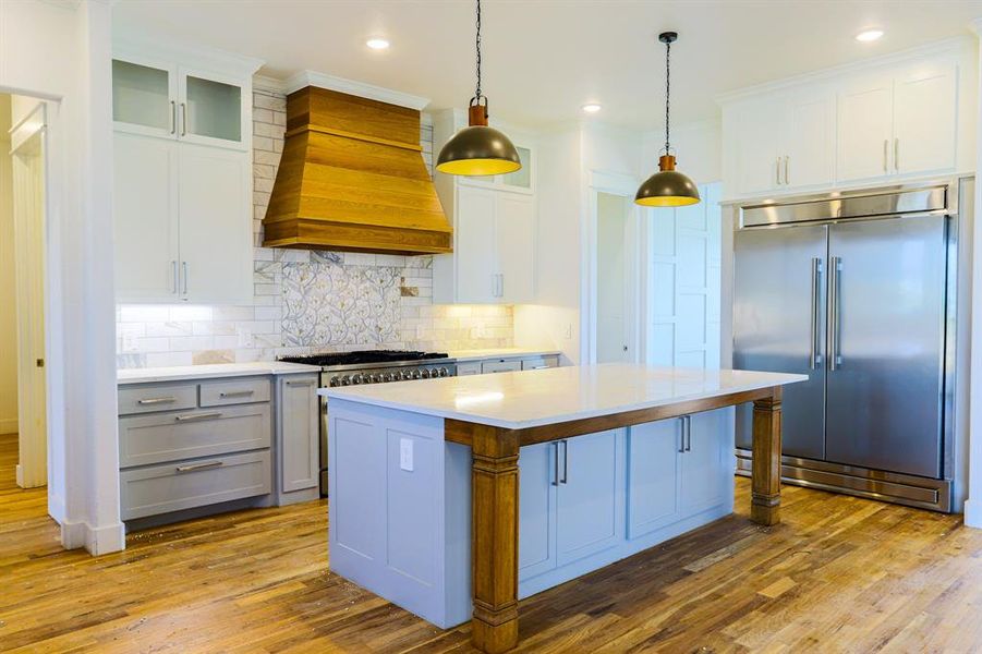 Kitchen with custom range hood, backsplash, a kitchen island, stainless steel appliances, and hardwood / wood-style flooring