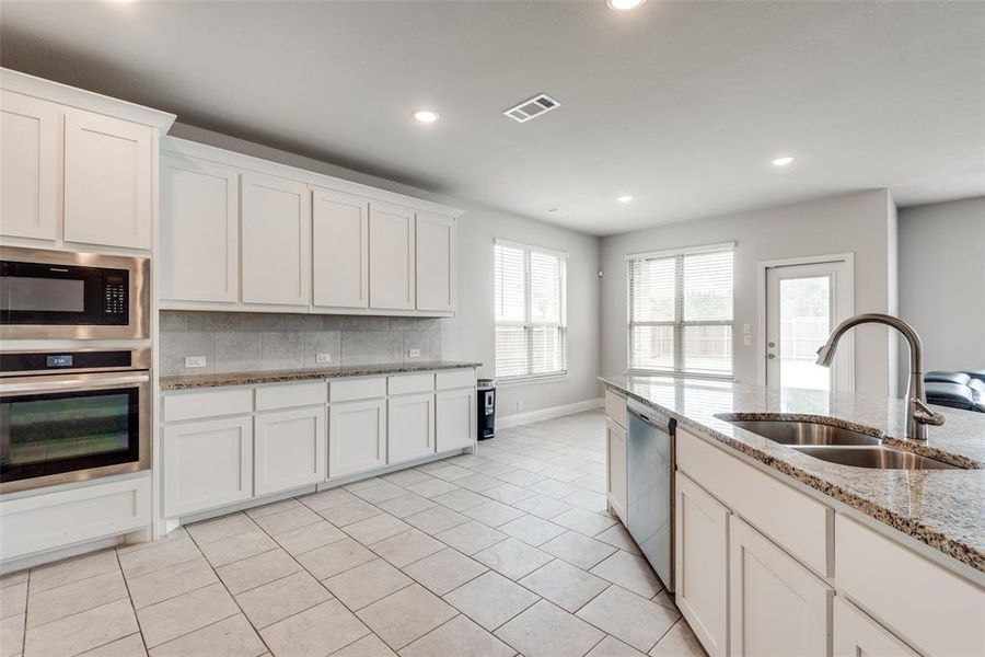 Kitchen featuring white cabinetry, tasteful backsplash, light stone countertops, stainless steel appliances, and sink