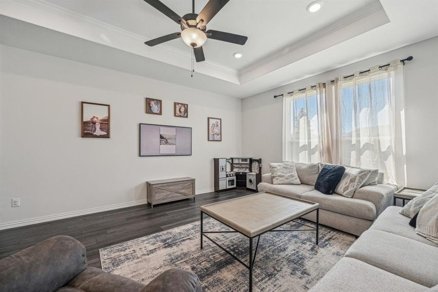 Living room with crown molding, hardwood / wood-style flooring, ceiling fan, and a tray ceiling