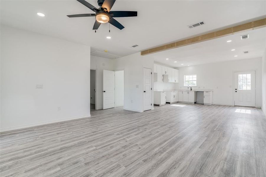 Unfurnished living room with beamed ceiling, ceiling fan, and light hardwood / wood-style flooring