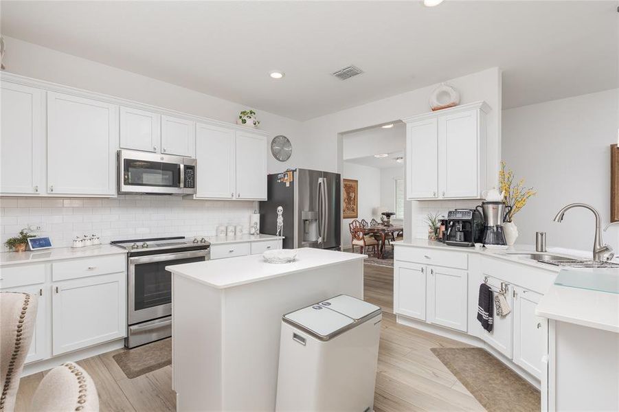 Kitchen with white cabinets, backsplash, appliances with stainless steel finishes, a center island, and light hardwood / wood-style floors