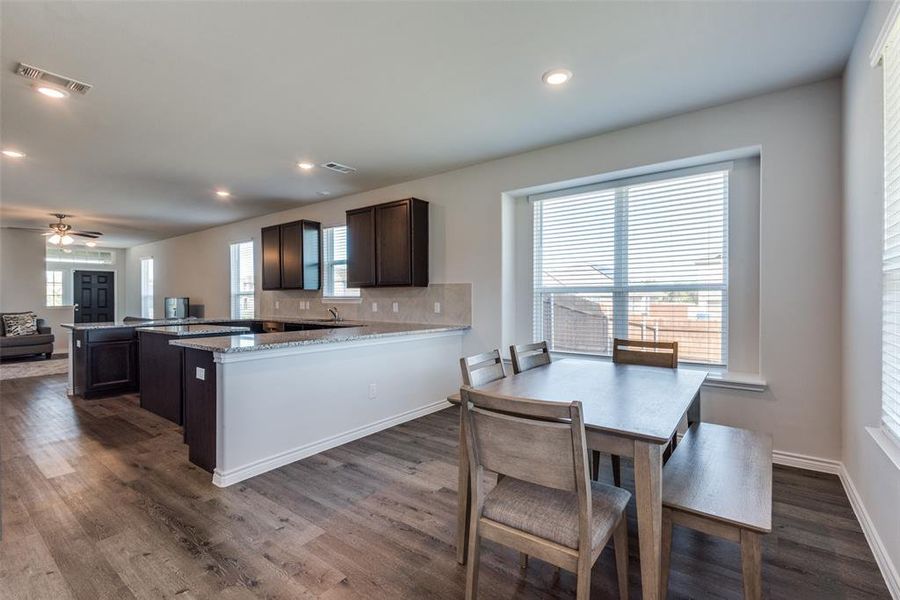 Kitchen with ceiling fan, kitchen peninsula, light stone countertops, dark hardwood / wood-style flooring, and decorative backsplash